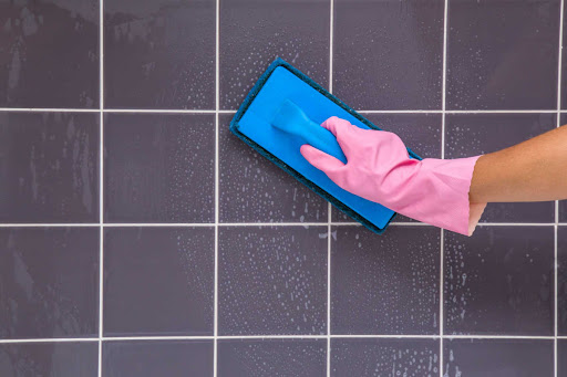 A woman wearing a pink glove is cleaning a tile. Her face is not shown.