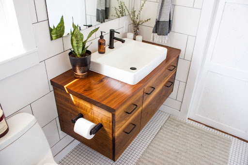 A bathroom with white tile walls and a white sink on a wooden vanity.